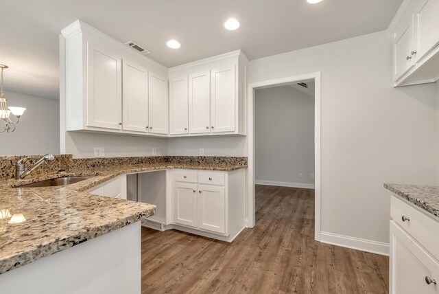 kitchen with light stone countertops, light wood-type flooring, sink, decorative light fixtures, and white cabinetry