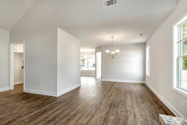 empty room with a wealth of natural light, dark hardwood / wood-style flooring, a chandelier, and vaulted ceiling