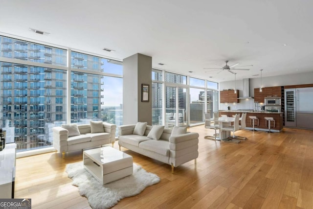 living room featuring light hardwood / wood-style flooring, expansive windows, ceiling fan, and a healthy amount of sunlight