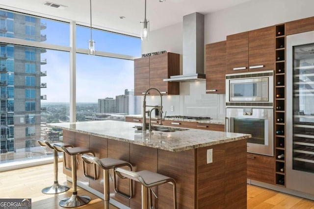 kitchen featuring visible vents, modern cabinets, stainless steel appliances, light wood-style floors, and wall chimney range hood