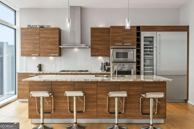 kitchen with light wood finished floors, built in appliances, modern cabinets, and wall chimney exhaust hood