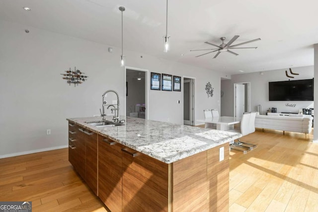 kitchen with light wood finished floors, open floor plan, a large island with sink, and a sink