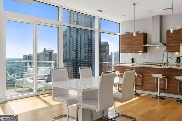 dining space featuring light wood finished floors, a city view, a wall of windows, and visible vents