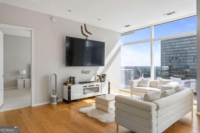 living room featuring floor to ceiling windows, light wood-style flooring, visible vents, and baseboards