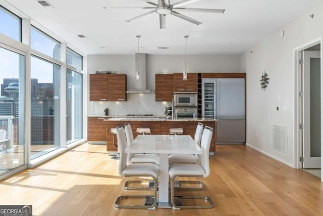 kitchen featuring visible vents, wall chimney range hood, built in appliances, brown cabinetry, and modern cabinets