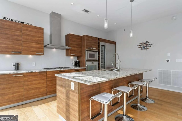 kitchen featuring visible vents, oven, a sink, stainless steel microwave, and wall chimney exhaust hood