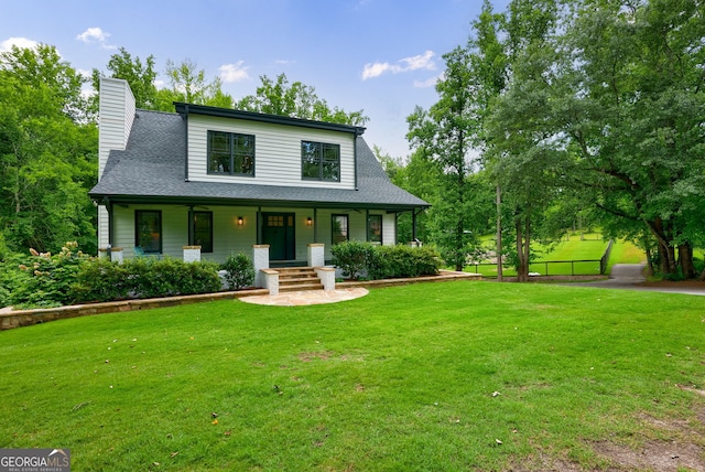 view of front of house featuring covered porch, a front lawn, a chimney, and a shingled roof