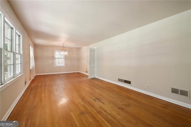 spare room featuring light wood finished floors, an inviting chandelier, baseboards, and visible vents