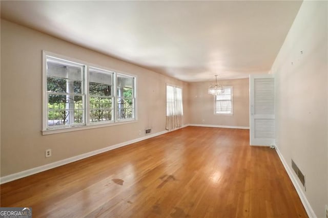 empty room featuring a notable chandelier, baseboards, visible vents, and light wood-style flooring
