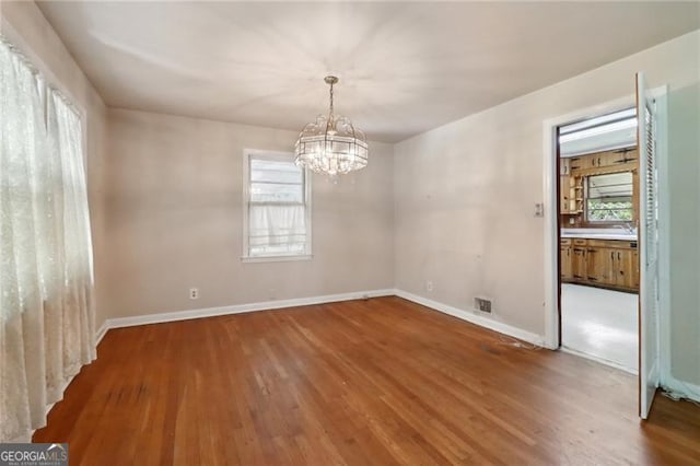 empty room featuring hardwood / wood-style floors, a wealth of natural light, and an inviting chandelier