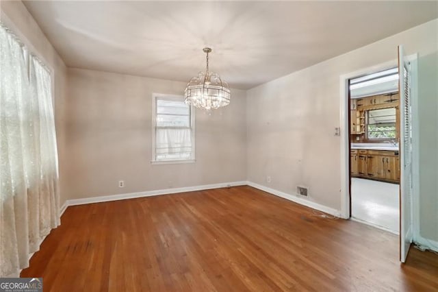 unfurnished dining area featuring a chandelier, baseboards, and wood finished floors