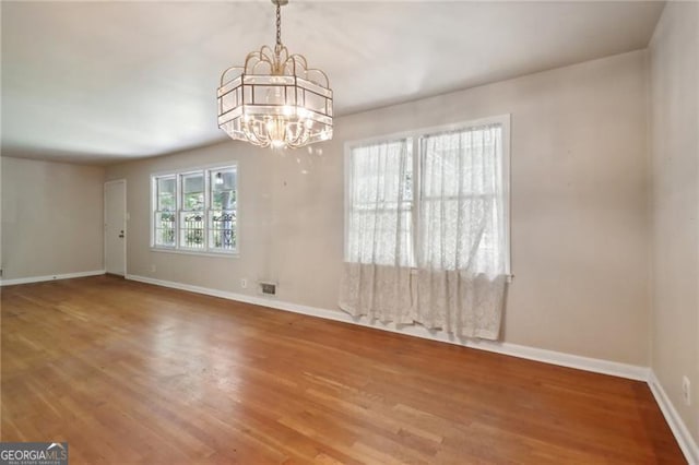 unfurnished dining area featuring wood finished floors, a notable chandelier, and baseboards
