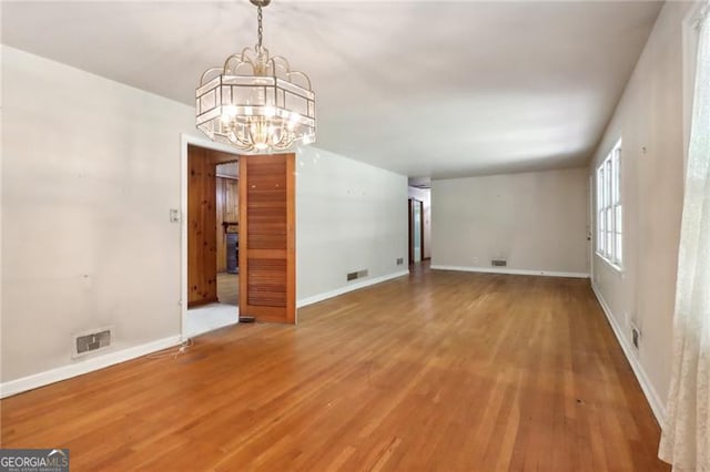 unfurnished dining area featuring visible vents, baseboards, a notable chandelier, and wood finished floors