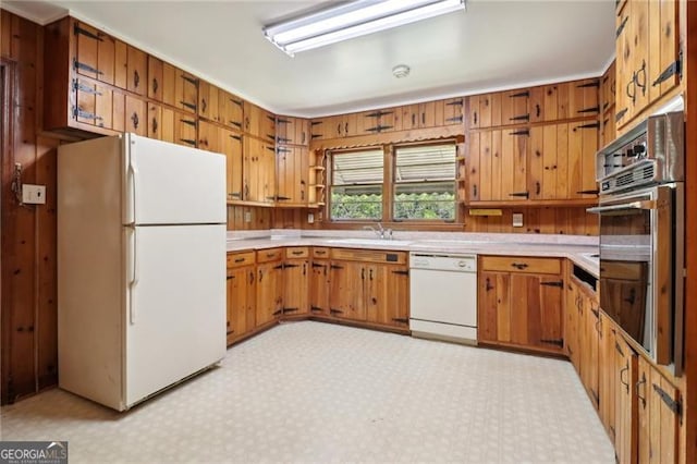 kitchen with white appliances, light countertops, brown cabinetry, light floors, and a sink