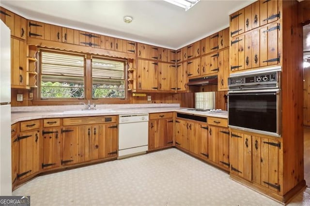 kitchen with white appliances, light countertops, under cabinet range hood, brown cabinets, and a sink