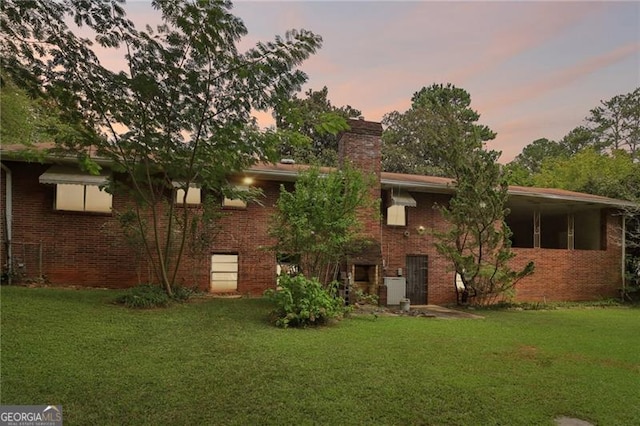 back of property at dusk featuring brick siding, a chimney, and a lawn