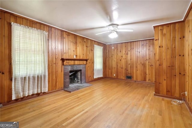 unfurnished living room featuring ceiling fan, a fireplace, light hardwood / wood-style flooring, and wooden walls