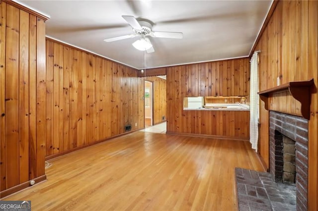 unfurnished living room with a fireplace, ceiling fan, wooden walls, and hardwood / wood-style floors