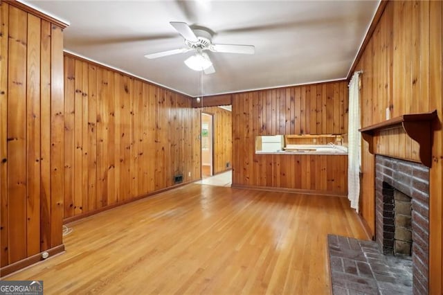 unfurnished living room featuring a fireplace, wooden walls, light wood-style floors, and ceiling fan