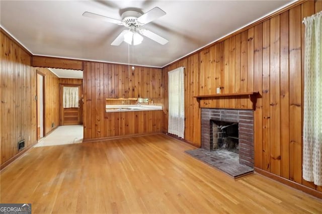unfurnished living room featuring wooden walls, a brick fireplace, visible vents, and wood finished floors