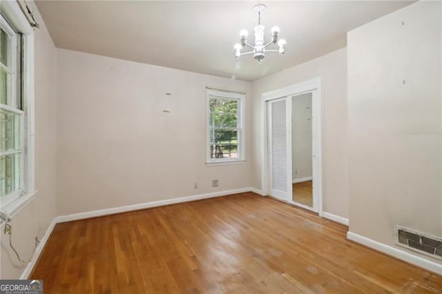 unfurnished bedroom with visible vents, baseboards, a closet, a notable chandelier, and wood finished floors