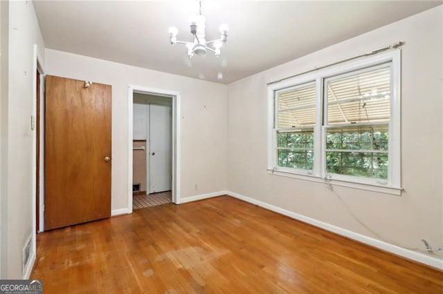 unfurnished bedroom featuring a notable chandelier, baseboards, visible vents, and wood finished floors