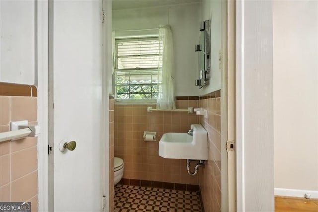 bathroom featuring toilet, a sink, a wainscoted wall, and tile walls