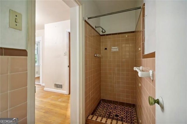 bathroom with a tile shower, wood finished floors, and visible vents