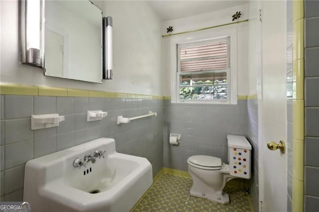bathroom featuring tile patterned floors, toilet, wainscoting, tile walls, and a sink