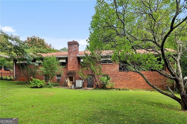back of property with a yard, brick siding, and a chimney