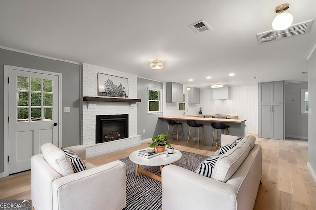 living room featuring a brick fireplace, ornamental molding, sink, and light hardwood / wood-style floors