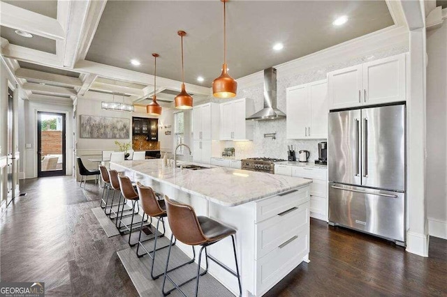 kitchen featuring a kitchen island with sink, premium appliances, light stone countertops, white cabinets, and wall chimney range hood