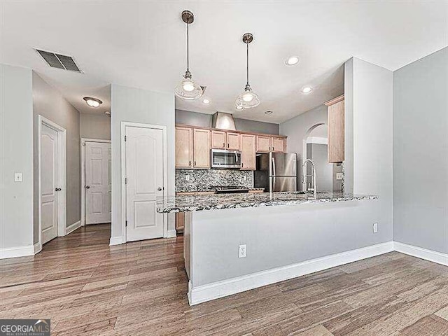 kitchen with backsplash, light brown cabinetry, wood-type flooring, decorative light fixtures, and stainless steel appliances