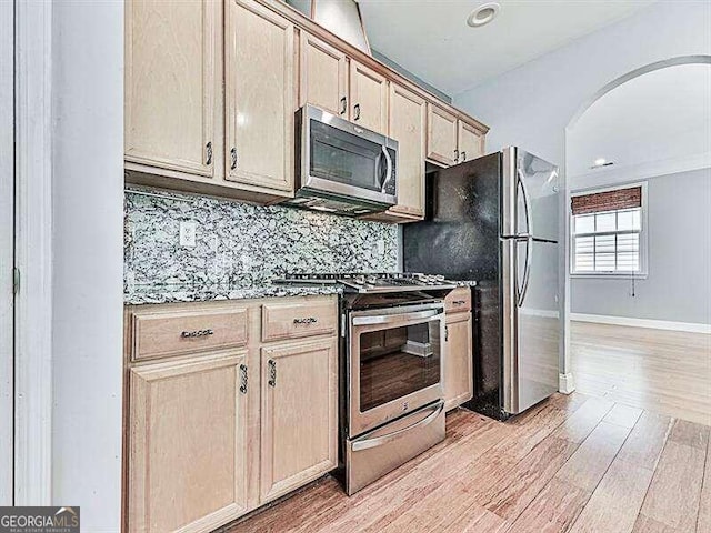 kitchen featuring light wood-type flooring, appliances with stainless steel finishes, decorative backsplash, light brown cabinets, and lofted ceiling