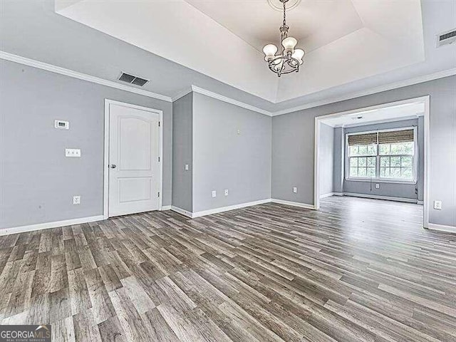 unfurnished living room with a tray ceiling, crown molding, hardwood / wood-style floors, and an inviting chandelier