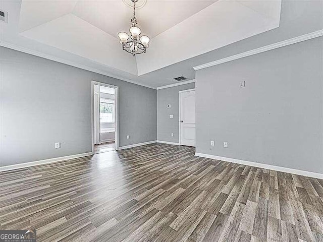 empty room with hardwood / wood-style floors, a raised ceiling, an inviting chandelier, and crown molding