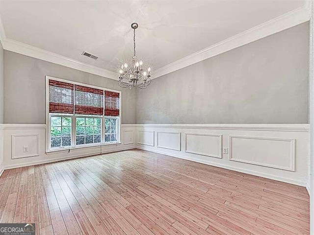 empty room with light wood-type flooring, ornamental molding, and a chandelier