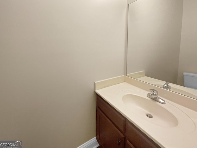 half bath featuring baseboards, vanity, and toilet