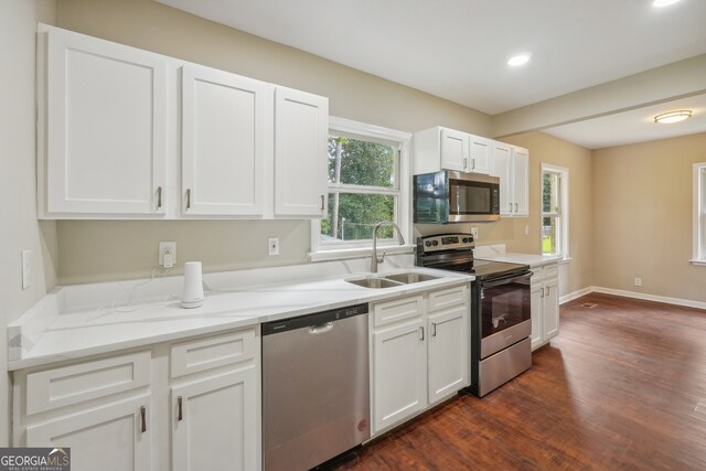 kitchen featuring dark wood-type flooring, white cabinets, appliances with stainless steel finishes, light stone counters, and sink