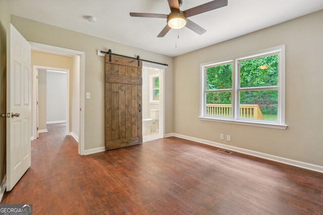 unfurnished bedroom with multiple windows, a barn door, hardwood / wood-style floors, and ceiling fan