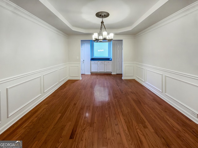 unfurnished dining area featuring an inviting chandelier, a raised ceiling, dark wood-style flooring, and a decorative wall