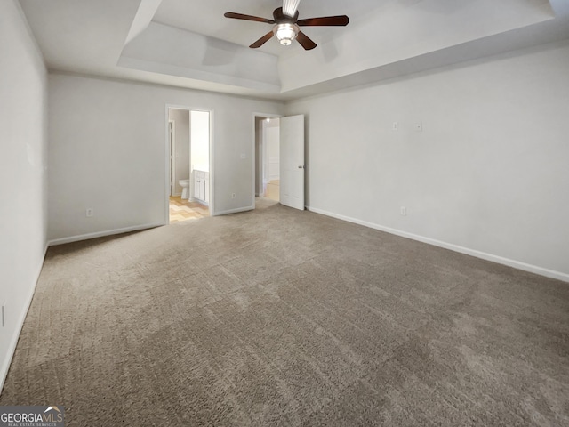 empty room featuring baseboards, a raised ceiling, a ceiling fan, and light colored carpet