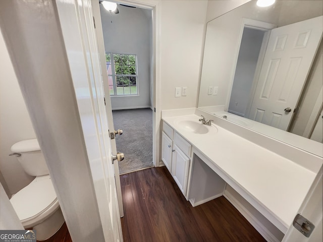 half bathroom with toilet, baseboards, wood finished floors, and vanity