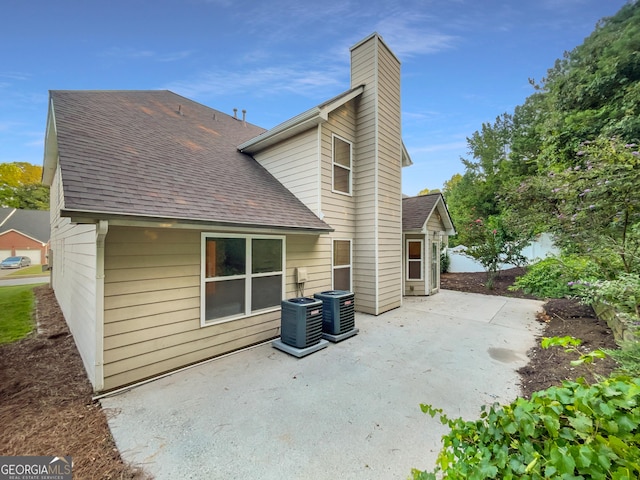 rear view of house with a shingled roof, a patio area, a chimney, and central AC unit