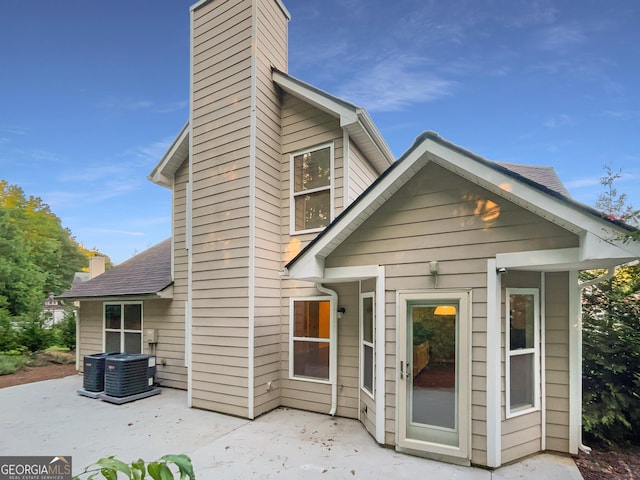 back of property featuring a shingled roof, a patio area, and a chimney