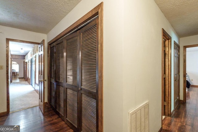 corridor with a textured ceiling and dark colored carpet