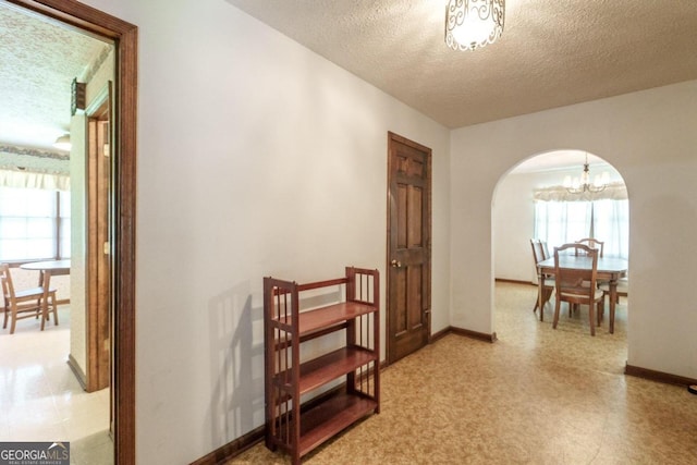 corridor with a notable chandelier and a textured ceiling