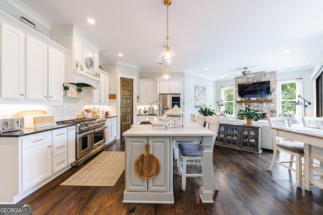 kitchen with double oven range, white cabinetry, an island with sink, decorative backsplash, and decorative light fixtures