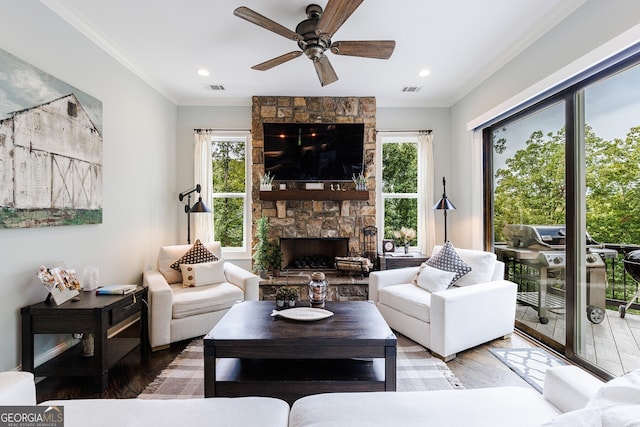 living room featuring hardwood / wood-style floors, ornamental molding, a stone fireplace, and a healthy amount of sunlight