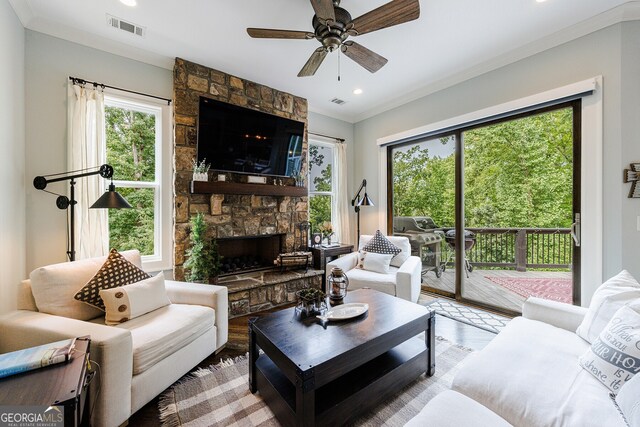 living room featuring ceiling fan, ornamental molding, wood-type flooring, and a stone fireplace